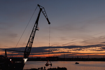 Fototapeta premium The silhouette of a construction crane at sunset against the river