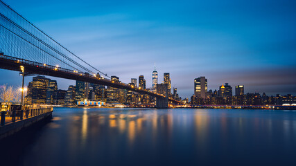 Blue hour long exposure panorama of Brooklyn Bridge and Lower Manhattan Skyline/One World Trade Center against epic night sky, Dumbo, New York City