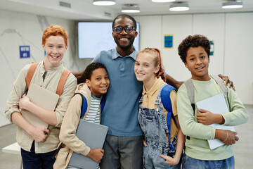 Portrait of male African-American teacher posing with diverse group of children in class and...