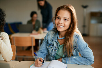 Happy high school student writes during class and looks at camera.