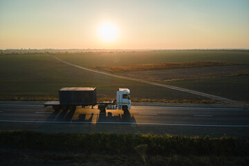 Fototapeta premium Aerial view of blurred fast moving semi-truck with cargo trailer driving on highway hauling goods in evening. Delivery transportation and logistics concept