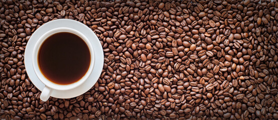 white cup filled with coffee on a background of coffee beans. long banner. view from above