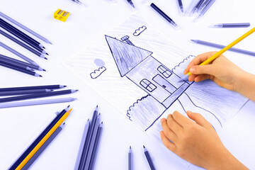 Child girl draws house with multicolored felt-tip pens on a white sheet. Color of 2022 year