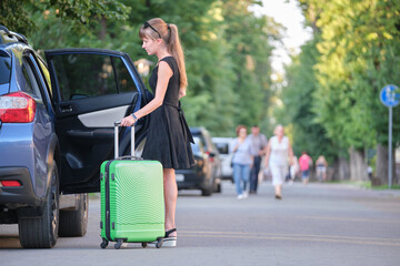 Young woman driver taking out suitcase bag out of her car. Travelling and vacations concept
