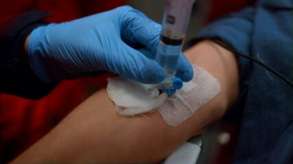 Medical worker in gloves inserting iv fluids into patient arm with catheter