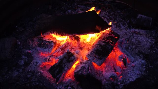 Campfire outside in a pit; close up of exterior campfire, in it's last stages before dying out. Orange flames, purple embers, ash. 623 
