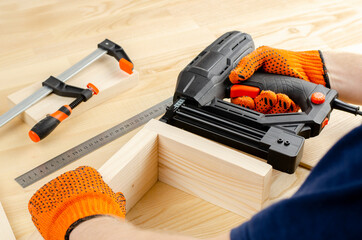 Electric stapler. Iron clamps. Squeeze wooden blocks. Hands in work gloves. Tool in the workshop....