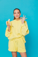 beautiful woman in yellow clothes eating a banana on a blue background