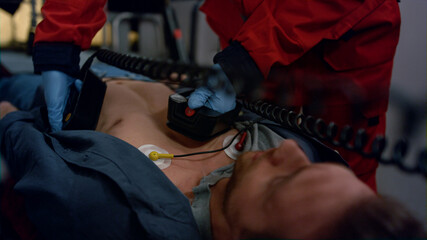 Doctor rescuing patient with external defibrillator. Paramedic reanimating man