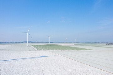 Fototapeta na wymiar Four wind turbines in the middle of a snowy field in Europe, France, Normandy, between Dieppe and Fecamp, in Winter, on a sunny day.