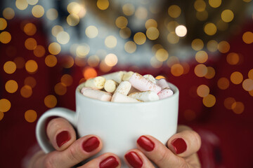 Woman's hands holds a cup of hot chocolate or cocoa with marshmallows. Holiday atmosphere and warming hot drink in winter. Close-up. Selective focus.