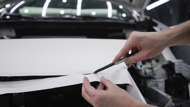Detailing the car. The master cuts the film on the machine with a knife. Retrofitting the car with a white protective film, the master makes a cut in the coating with a knife, protecting the cars from