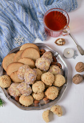 Three kinds of cookies, nuts, tea in a glass cup, a warm blue scarf on a white table. View from above.
