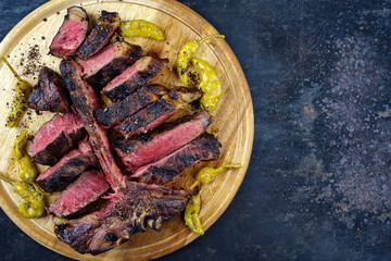 Traditional barbecue dry aged wagyu porterhouse beef steak bistecca alla Fiorentina sliced and served with pepperoni as top view on a rustic wooden board with copy space right