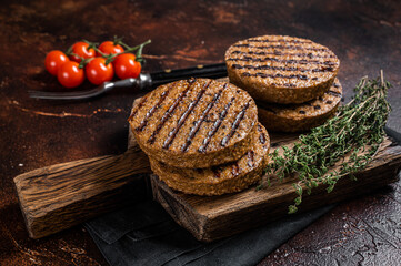 Fototapeta na wymiar BBQ Grilled plant based meat burger patties, vegan cutlets on wooden board with herbs. Dark background. Top view