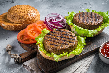 Plant based meatless burgers with vegan grilled pattie, tomato and onion on a wooden serving board. Gray background. Top view - obrazy, fototapety, plakaty