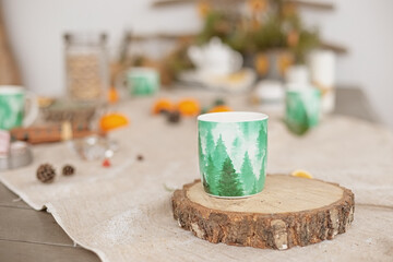 Winter table decor outside, on a linen tablecloth there is a green mug of hot drink on a tree cut