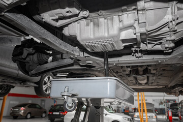 Male mechanic changing the oil of a vehicle on a car lift.