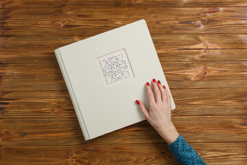 beige photo book with fabric cover. stylish wedding photo album. a person opens a photobook.  womans hand holding a family photoalbum on wooden background with copy space for text
