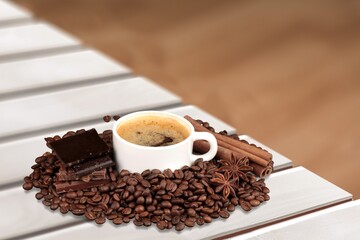 In front of a wall, on a desk, a cup of turkish coffee,  beans.