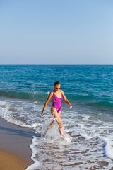 A young beautiful woman with a toned body in a bright swimsuit walks along the sandy beach. Summer vacation at the sea. Mediterranean Turkish Sea. Selective focus