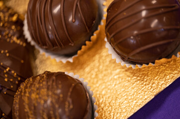 close up of sweet chocolate balls in paper wrapping resting on golden foil paper