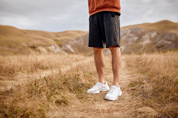 Cropped male in shorts and sneakers stand on grass, calm, no motion. jogger runner sportsman take a...