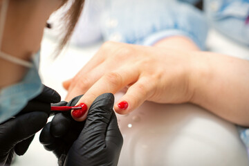 Painting nails of a woman. Hands of Manicurist in black gloves applying red nail polish on female Nails in a beauty salon