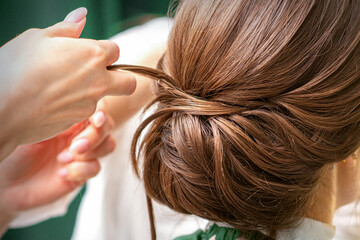 Naklejka premium Professional hairdresser doing hairstyle for a beautiful brunette young woman with long hair. Concept of fashion and beauty