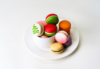 Colorful festive Christmas theme color French Macarons on white ceramic plate over clean background with copy space. Celebrate Thanksgiving, Xmas, New Year Party Concept. Modern setting. Bright light.