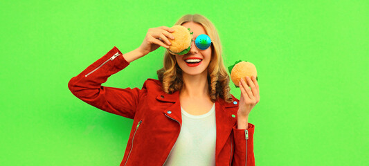 Portrait of stylish happy smiling young woman eating tasty big burger fast food on green colorful...