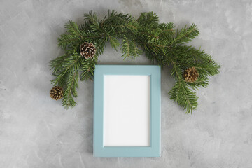 New year mockup: christmas tree branches with blue photo frame on grey background. Holidays concept. Text space