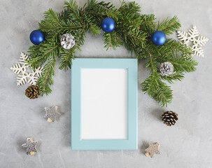 New year mockup: decorated christmas tree branches with blue photo frame on grey background. Holidays concept. Text space