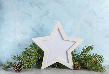 New year mockup: christmas tree branches with white star shaped photo frame on blue background. Holidays concept. Text space