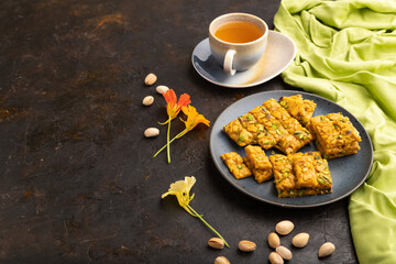Traditional iranian dessert sohan with cup of green tea on a black concrete background. side view, copy space.
