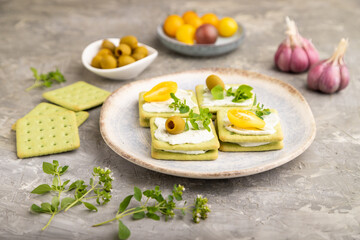 Green cracker sandwiches with cream cheese and tomatoes on gray concrete background. side view, close up.