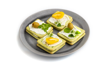 Green cracker sandwiches with cream cheese and tomatoes on gray plate isolated on white background. side view