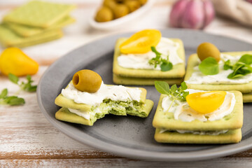 Green cracker sandwiches with cream cheese and cherry tomatoes on white wooden background. side view, selective focus.