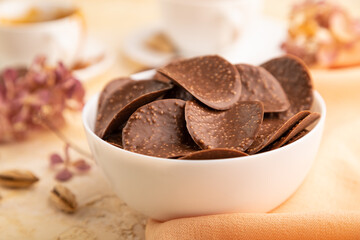 Chocolate chips with cup of coffee on a beige concrete background. side view, close up, selective focus.