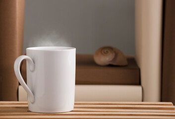 white cup of coffee with hot steam, on the desk with nautilus shell and books, grey background