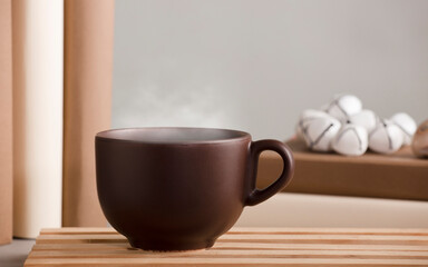 white cup of coffee with hot steam, on the desk with shells and books, grey background