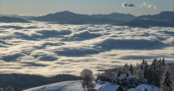 Time lapse of inversion clouds moving in alpine valley. Beautiful landscape in winter season. Small village in the mountains in Slovenia. Low moving fog with long shadows. Aerial or elevated view