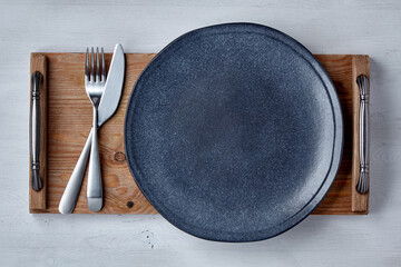 Empty ceramic dark plate with cutlery on a brown wooden tray