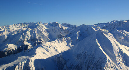 Fototapeta na wymiar survol, vue d'avion d'une superbe chaine montagneuse enneigé sous le soleil avec un ciel bleu 