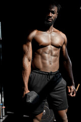 Fototapeta na wymiar powerful strong sweaty focused fit muscular man with big muscles holding heavy dumbbell for cross fit training, african man do hard core workout in dark modern gym, real people exercising. portrait