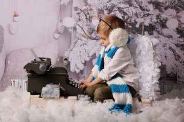 A little boy wearing white blue stripes long scarf, white ear muffs and angel wings writing letter...
