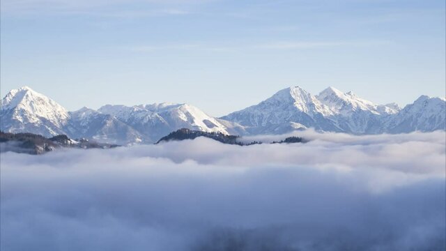 Low inversion clouds moving in alpine valley. Time lapse of fog covering amazing landscape in winter. Snowy mountains in the distance. Pristine nature in Slovenia, Europe. Sunrise. Right tracking