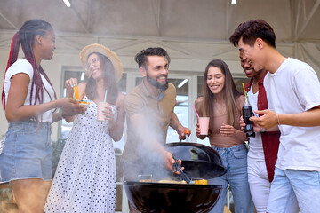 Multiracial group of friends drinking beverages at summer evening, cooking barbecue bbq. Multiethnic friends having fun, enjoying weekends. Interracial group of people in casual wear relaxing