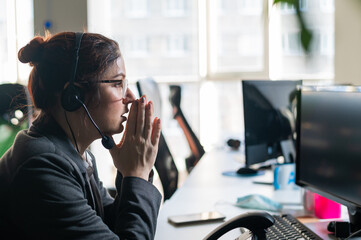 Portrait of woman in headset in frustration holds hands by face in office.