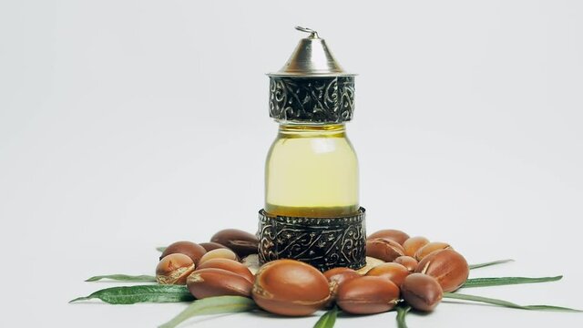 Argan oil in a oriental glass and metal bottle and argan nuts with green leaves motion on white background.